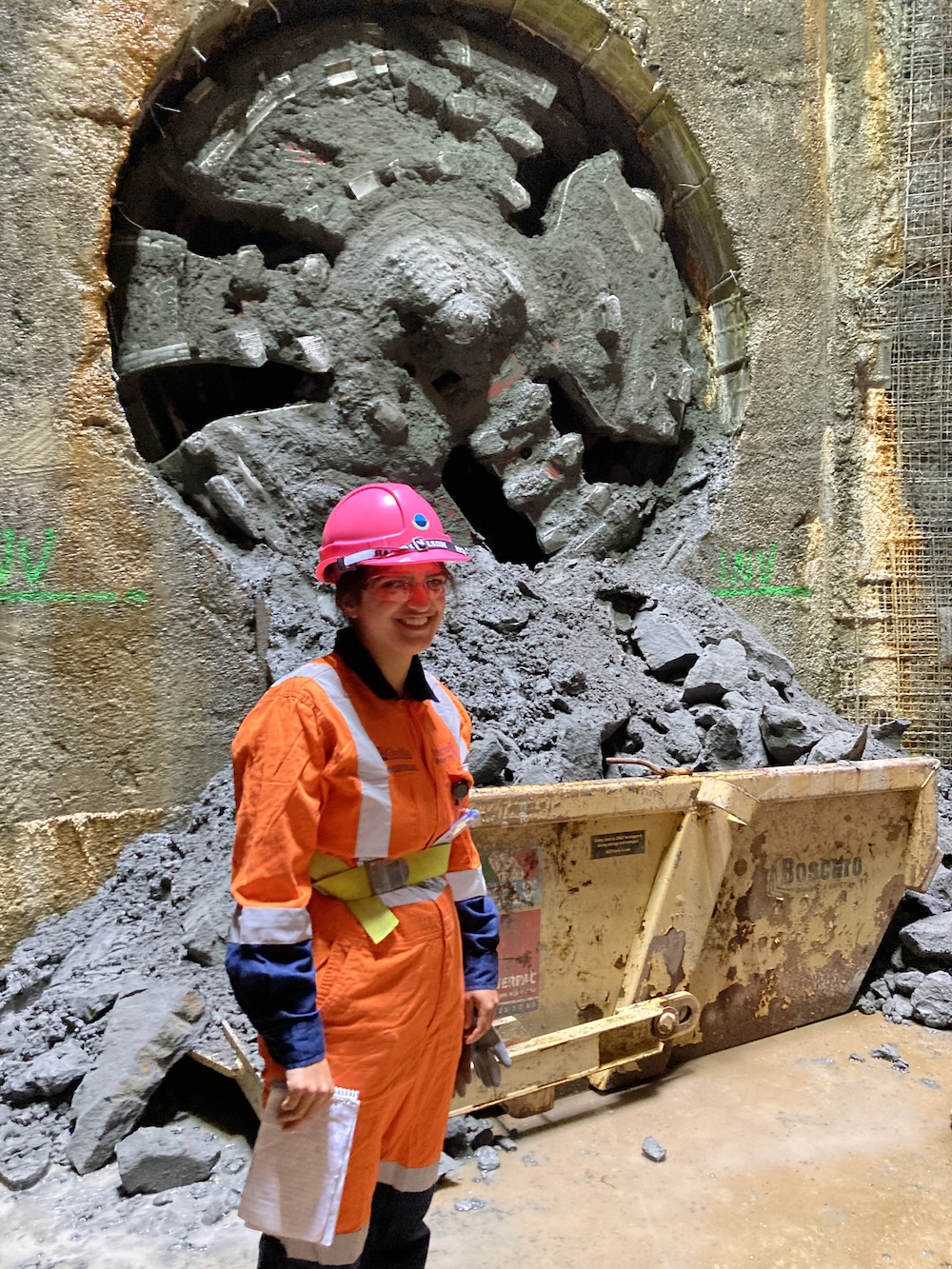 Shanti on the job at a tunnel boring machine site thirty metres underground, wearing a hi vis boilersuit looking chuffed